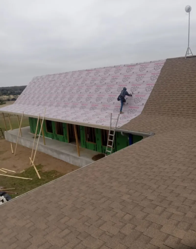 Worker preparing underlayment for a metal roof installation in Phelps